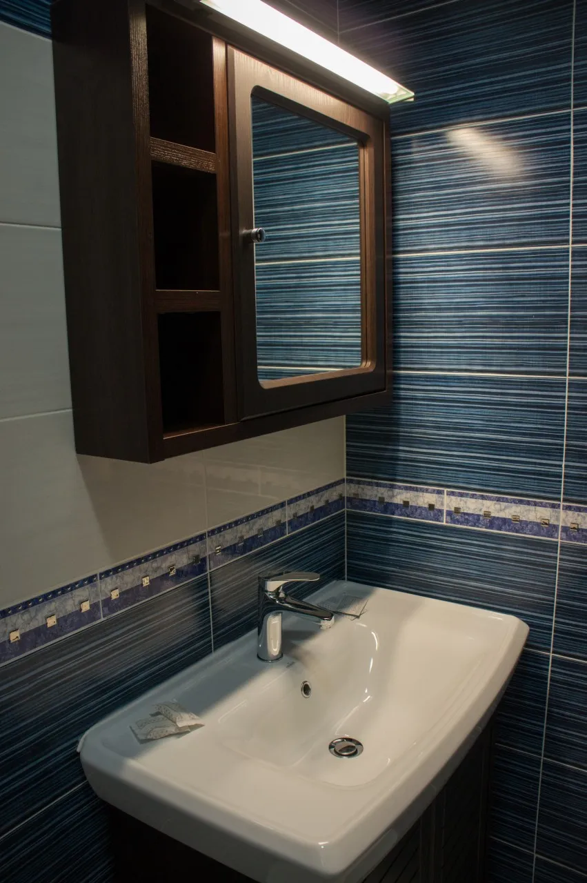 A white washbasin and a mirrored cabinet against a blue-tiled wall