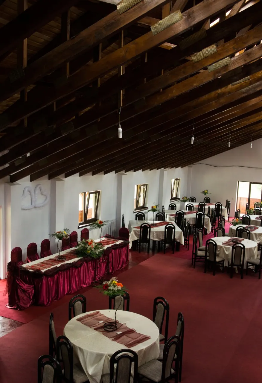 The events hall under its beamed ceiling, with the long table dressed in burgundy satin and round tables set with flower arrangements.