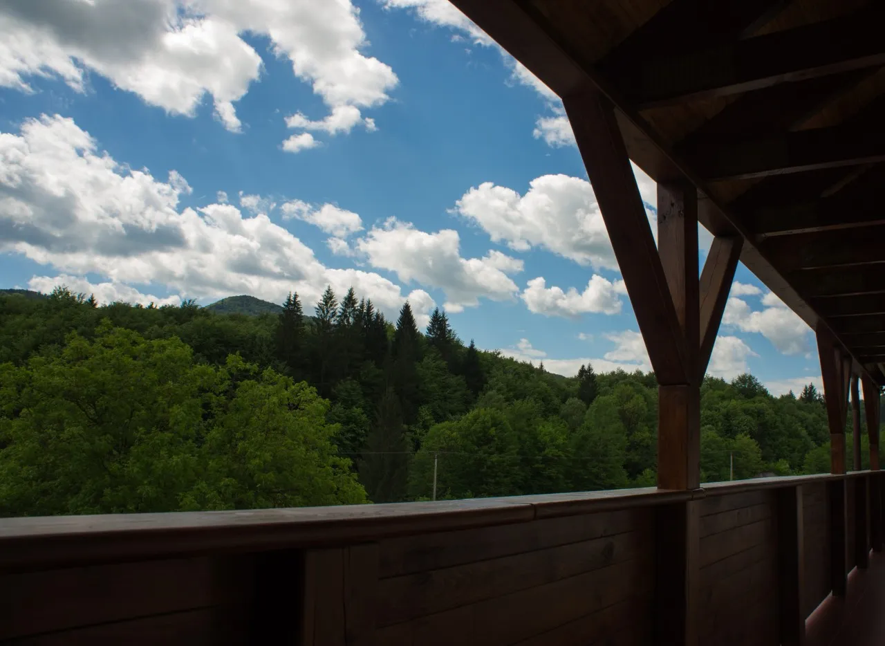 A covered balcony with wooden posts, open towards the wooded hills
