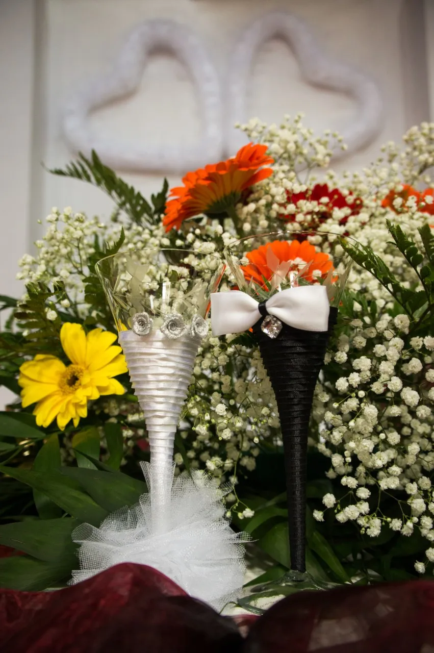 A flower arrangement of orange and yellow gerberas and white blooms, beside glasses tied with white ribbon.