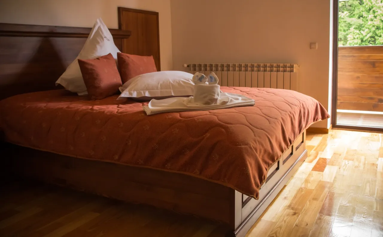 A double bed with a terracotta bedspread, beside the balcony door