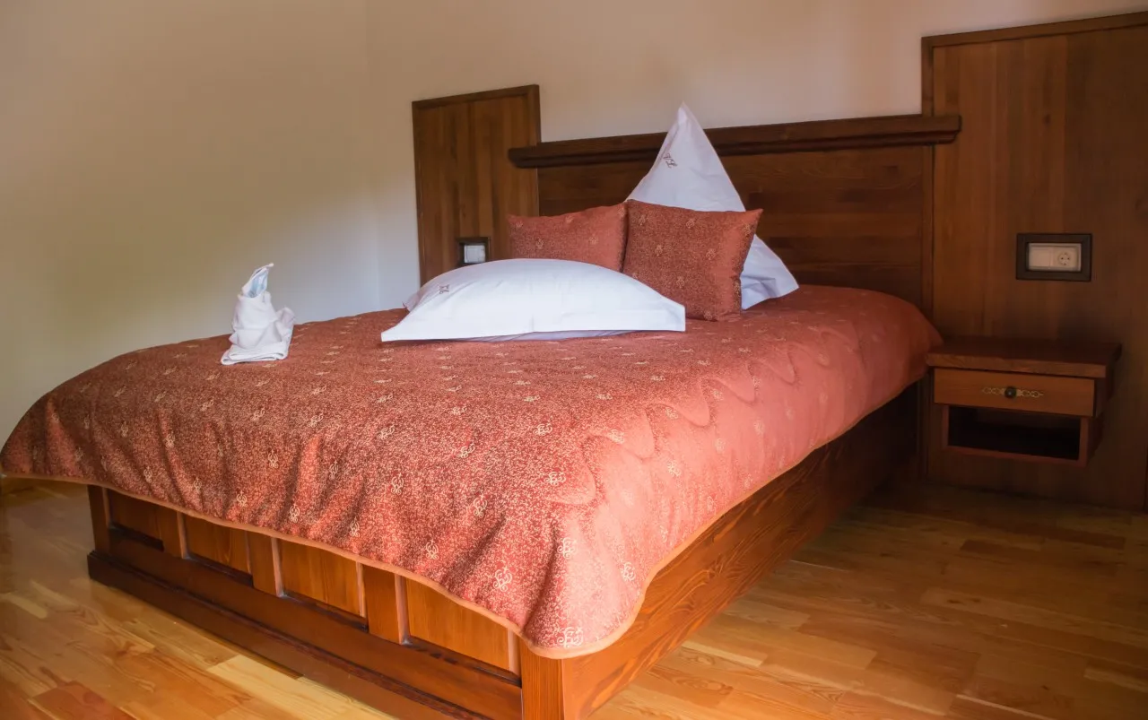 A double bed with a tall dark wooden headboard and a terracotta bedspread