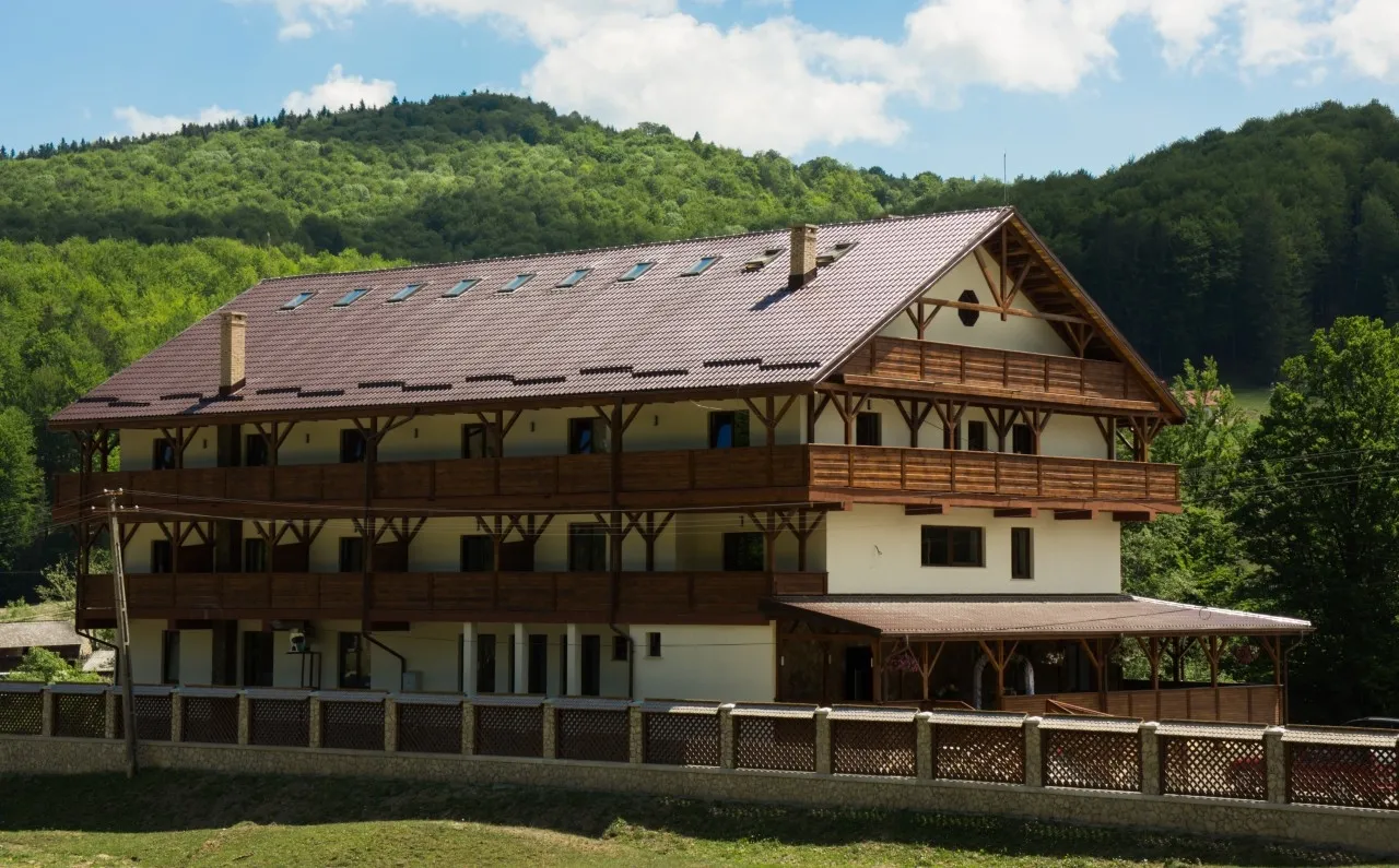 Cabana Vitoria Lipan seen at an angle, with timber balconies across three storeys, a stone-and-timber fence in the foreground and the wooded hill behind.
