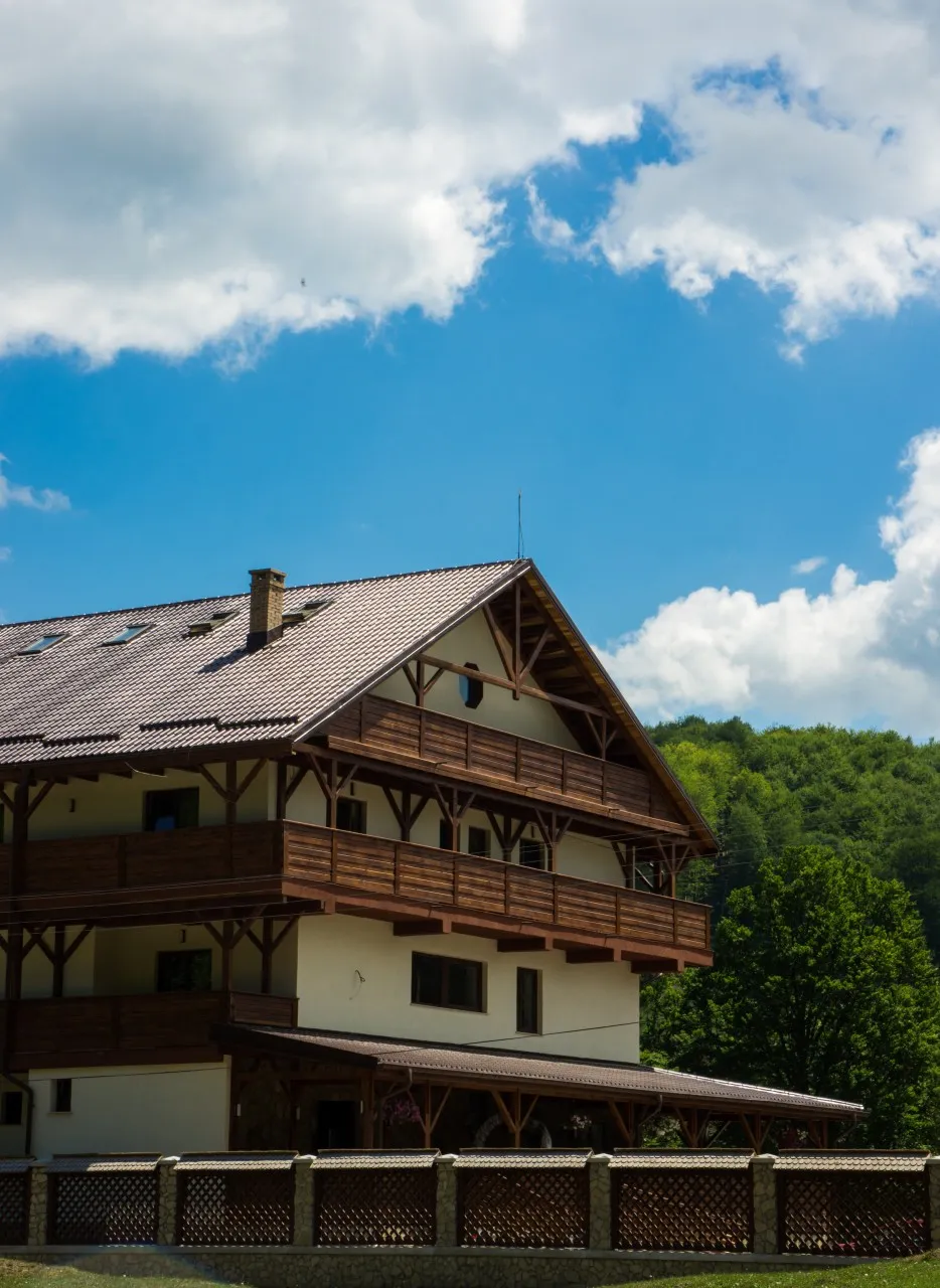The end of the chalet, with its steep roof and timber balconies, under a sky of white clouds.