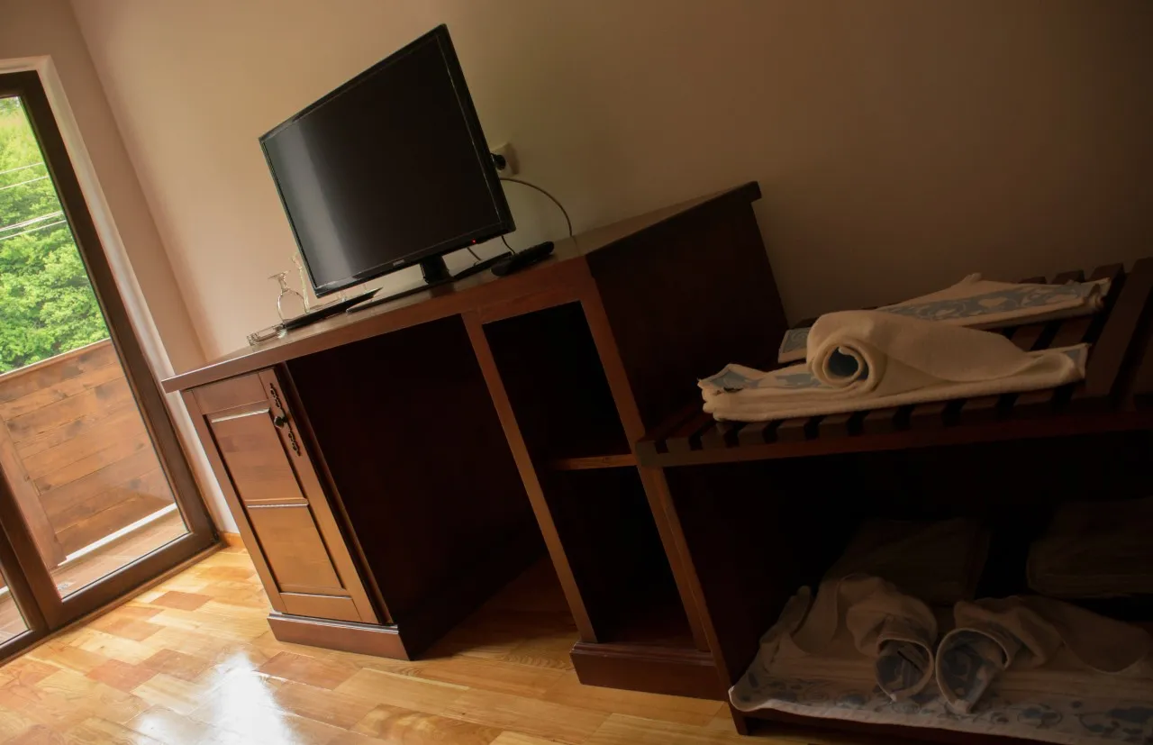 A TV on a dark wooden shelf unit, with folded towels beside it, on a wooden floor